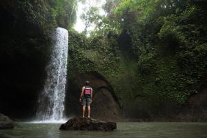 ウブドにあるMade Sura Bali Driver & Tourの滝の前の岩に立つ男 +3枚の写真
