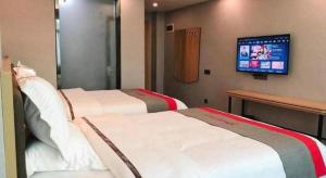 two beds in a hotel room with a tv on the wall at Jun Hotel Guangdong Zhanjiang Xiashan South Railway Station in Zhanjiang