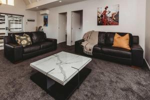 a living room with two leather couches and a glass table at Love It On Lemon - modern townhouse near CBD in New Plymouth