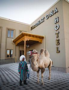 a person with a camel in front of a building at Hotel FAROHAT ONA in Khiva