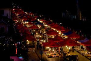 a market with red umbrellas and lights at night at We House River View Hotel And Travel in Luang Prabang