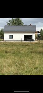 een witte schuur met een zwart dak in een veld bij Domek na Kaszubach u Doroty 