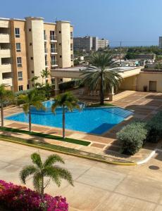 a swimming pool with palm trees and a building at Apartmento Minutos Caracola Beach in Porlamar