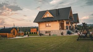 a wooden house with a black roof on a yard at Dziki Raj - domki z widokiem na Tatry oraz Babią Górę in Jabłonka