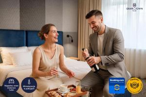 a man and a woman sitting on a bed with a bottle of champagne at Grape Town Hotel - Park79 in Zielona Góra