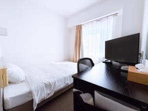 a hotel room with a bed and a desk with a television at Uwajima Oriental Hotel in Uwajima