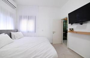 a white bedroom with a large bed and a flat screen tv at אחוזת סנטוריני - וילה מהממת עם בריכה מחוממת וג'קוזי בעין יעקב in ‘Ein Ya‘aqov +22 photos
