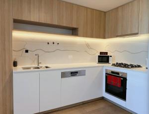 une cuisine avec des armoires blanches et un four à plaques de cuisson dans l'établissement Arnold Box Hill - Modern 2bed Apartment, à Box Hill