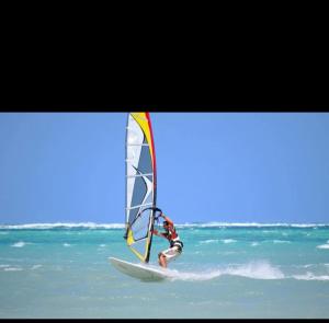 a person on a surfboard with a sail on the ocean at Diani's Little Gem in Ukunda