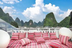 een groot bed met kussens op een balkon met uitzicht op de bergen bij 妙酒店阳朔西街漓江店 in Yangshuo