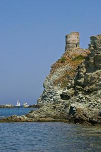 a castle on a rocky island in the water with a sailboat at Maison de charme avec Terrasse vue sur mer in Rogliano +8 photos