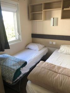 two beds in a room with a window at Mobilhome spacieux et calme in Pont-Aven