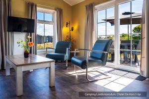 a living room with two chairs and a table and a room with windows at Camping Loodsmansduin in Den Hoorn