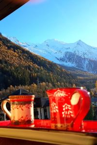 two red cups sitting on a window sill with snow covered mountains at Le Chamois 5E Balcon panoramique MontBlanc avec parking gratuit in Chamonix-Mont-Blanc