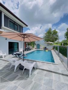 a swimming pool with an umbrella and chairs and a patio at Jazzy Pool Villa Hatyai in Hat Yai