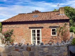 a brick house with a window behind a stone fence at Wilf's Barn, romantic cottage with free parking in Wedmore