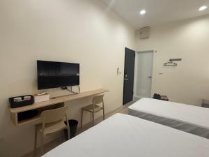 a bedroom with two beds and a desk with a television at Jian Guo Hotel in Pingtung City