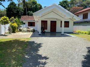 a small white house with a woman sitting in front of it at Hiri Relax Hostal in Dickwella