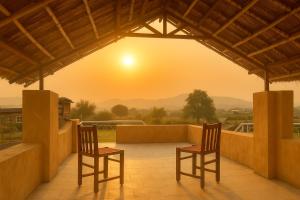two chairs on a balcony with a sunset in the background at IRWINA-In rhythm with nature in Pushkar
