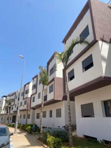 a building with palm trees in front of it at Appartement Moderne avec Piscine in Bouznika