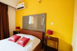 a bedroom with yellow walls and a bed with two red pillows at Résidence Bertille Abidjan Cocody in Abidjan +33 photos