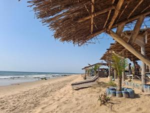 Una playa con una choza de paja y el océano. en Villa No Stress, en Somone
