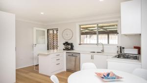 a white kitchen with white cabinets and a table at Oceanique in Old Bar
