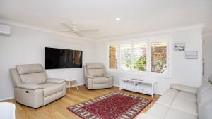 a living room with a couch and two chairs and a tv at Oceanique in Old Bar