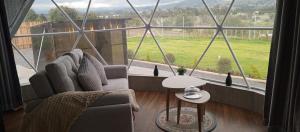 een woonkamer met een groot raam met een bank en een tafel bij La cabaña de Ciela Glamping con jacuzzi in Latacunga