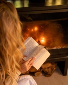 a woman reading a book in front of a fireplace at Lisine Lepo Mesto Guesthouse & Spa in Strmosten