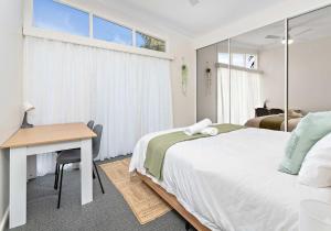 a bedroom with a bed and a desk and window at Coastal Palms - Family & Pet-Friendly Beachside Haven in Lake Illawarra
