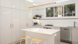 a kitchen with white cabinets and a sink and two stools at Summer Splendor - Ettalong Beach in Ettalong Beach