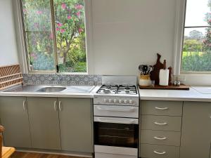a kitchen with a stove and a sink and two windows at Grandad's farmhouse in Northcliffe