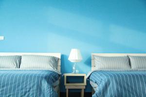 a blue bedroom with two beds and a night stand with a lamp at Little Weekend Inn in Jincheng