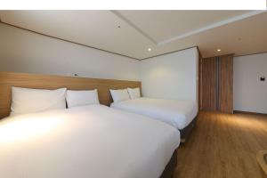 two beds in a hotel room with white sheets at Hotel Rest Seogwipo in Seogwipo