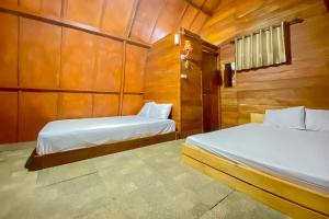 two beds in a room with wooden walls at Embun Lawu Cottage Tawangmangu in Sarangan