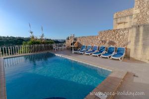 a swimming pool with lounge chairs next to a wall at Hibiscus in Xagħra