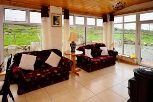 a living room with two chairs and a table and windows at Cottage 216 - Roundstone in Roundstone