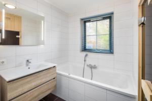 a white bathroom with a tub and a sink at Stuifzand Wellness Bungalow | 8 personen in Hooghalen +20 photos