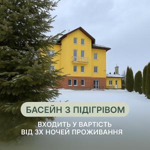 a yellow house in the snow with a tree at Вілла ЮРАН Східниця in Skhidnitsa