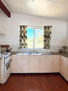 a kitchen with white cabinets and a large window at Marlins Beach Shack Broulee in Broulee