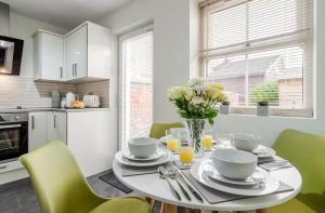 a white kitchen with a table with a vase of flowers at Ribby Stays - 2 bed Cottage Pet Friendly in Wrea Green +17 photos