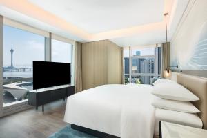 Un dormitorio con una gran cama blanca y un televisor de pantalla plana. en Courtyard by Marriott Zhuhai, en Zhuhai