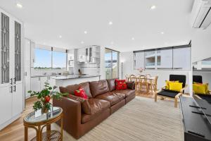 a living room with a brown couch and a kitchen at The Oceanfront Sanctuary Spa & Parking in Cronulla