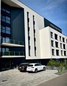 Dos coches estacionados en un estacionamiento frente a un edificio. en Horizon Park Lux II, en Boszkowo-Letnisko