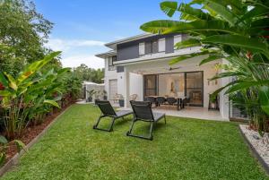 een huis met een gazon met twee stoelen en een tafel bij Argentea Cove - Poolside Escape near Palm Cove Beach in Palm Beach