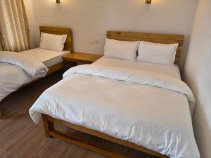 two beds in a room with white sheets at RJ Boutique Hotel - Ghandruk in Astam