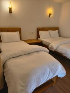 two beds in a room with white sheets at RJ Boutique Hotel - Ghandruk in Astam