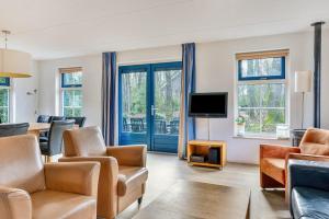 a living room with chairs and a tv and windows at Zandduin Wellness Villa | 10 personen in Hooghalen