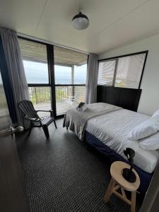 Un dormitorio con una cama, una silla y una ventana en Stanmore Bay Log Cabin - short walk to beach, en Stanmore Bay